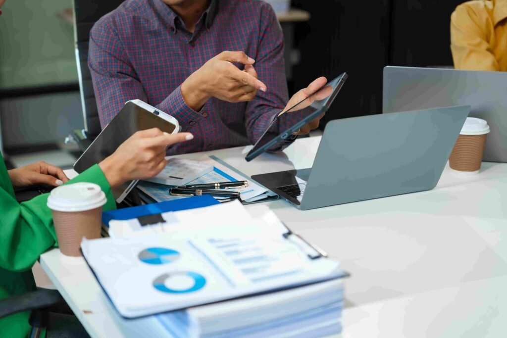 Team members reviewing financial documents with tablets and laptops at a meeting table