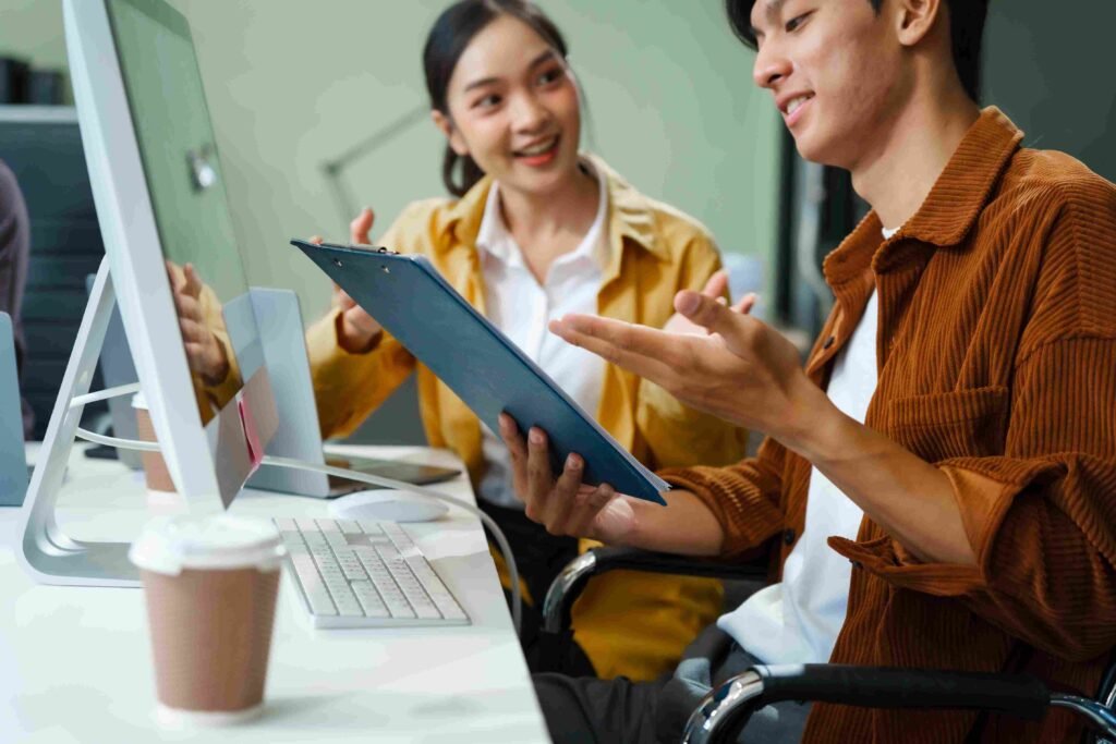 Two coworkers discussing documents beside a desktop computer in an office