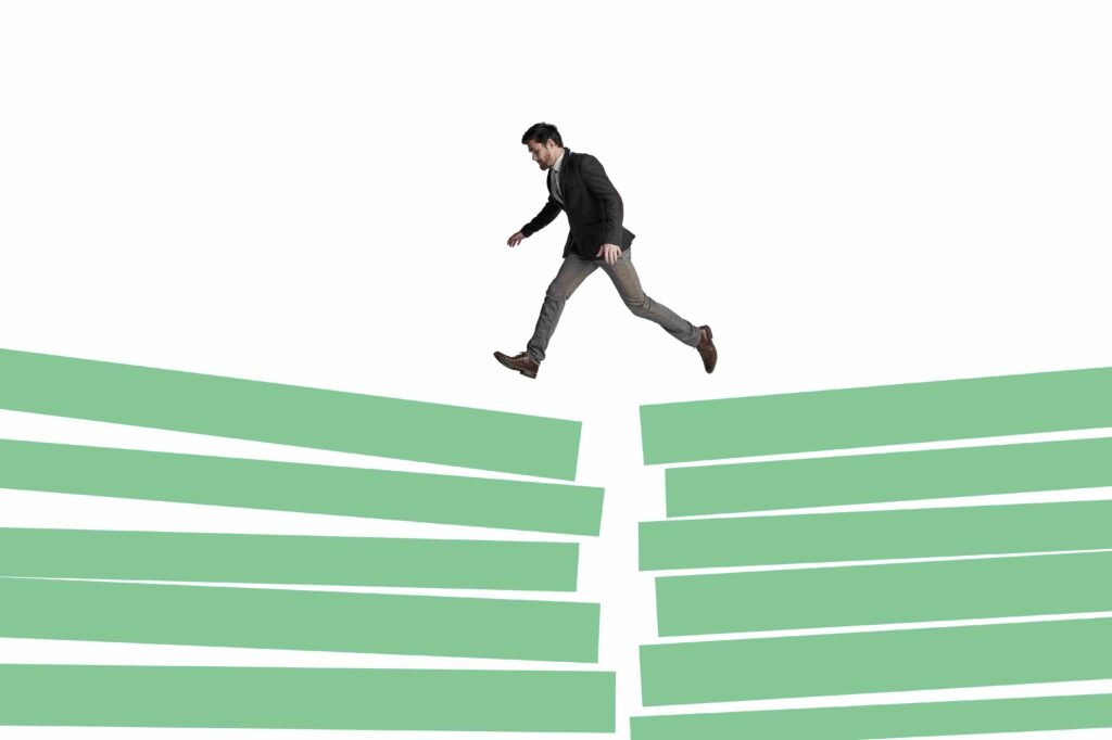 Businessman jumping across a gap between stacked green platforms