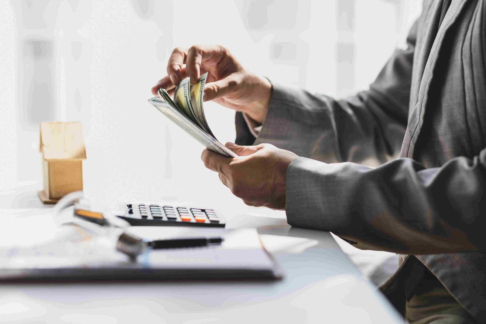 Businessperson counting cash at a desk beside a calculator and documents