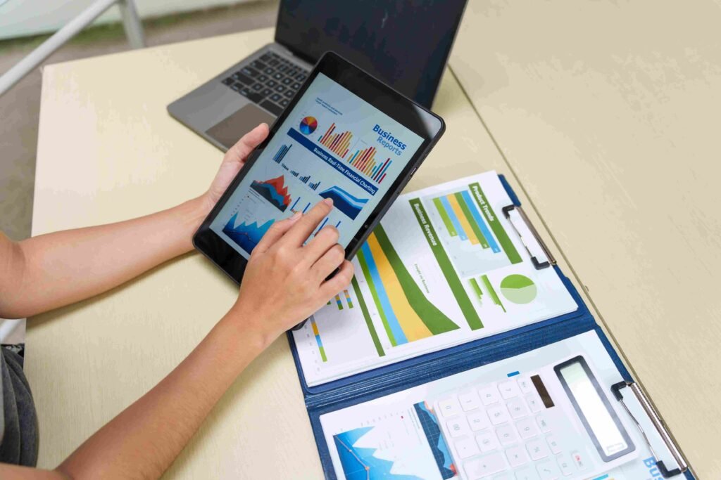 Person reviewing financial reports and charts on a tablet alongside printed business documents