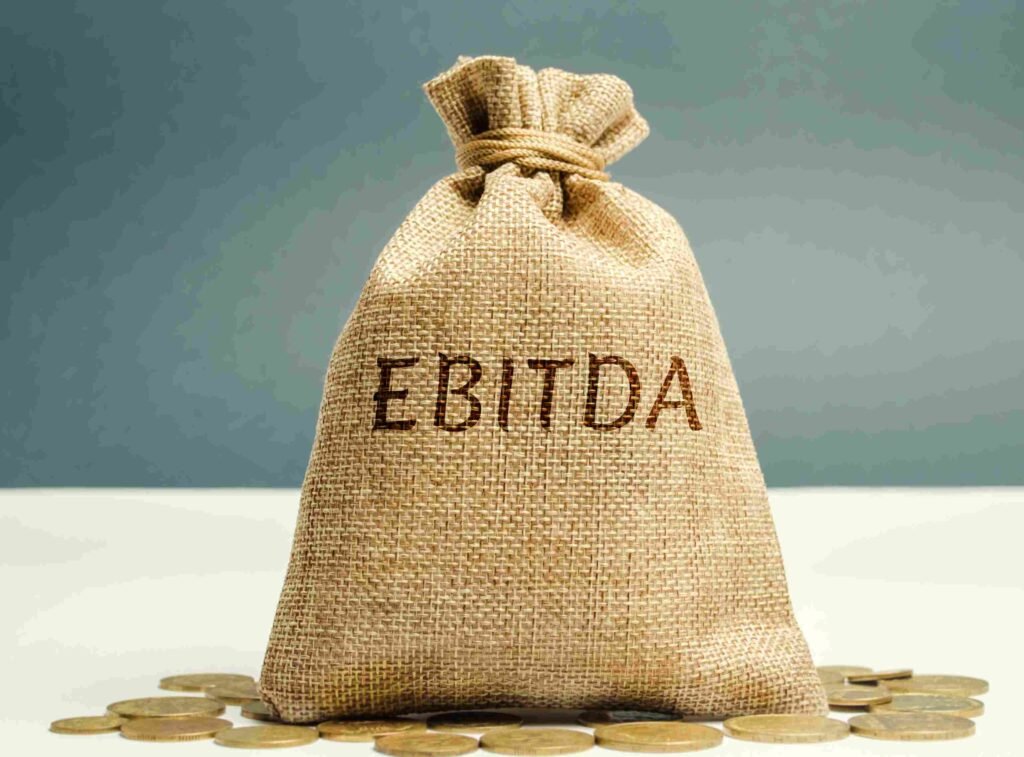 A sack labeled EBITDA sitting on a surface with coins scattered around it