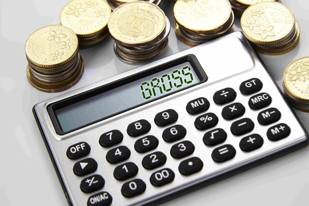 Calculator displaying gross figures next to stacks of coins representing business profit analysis