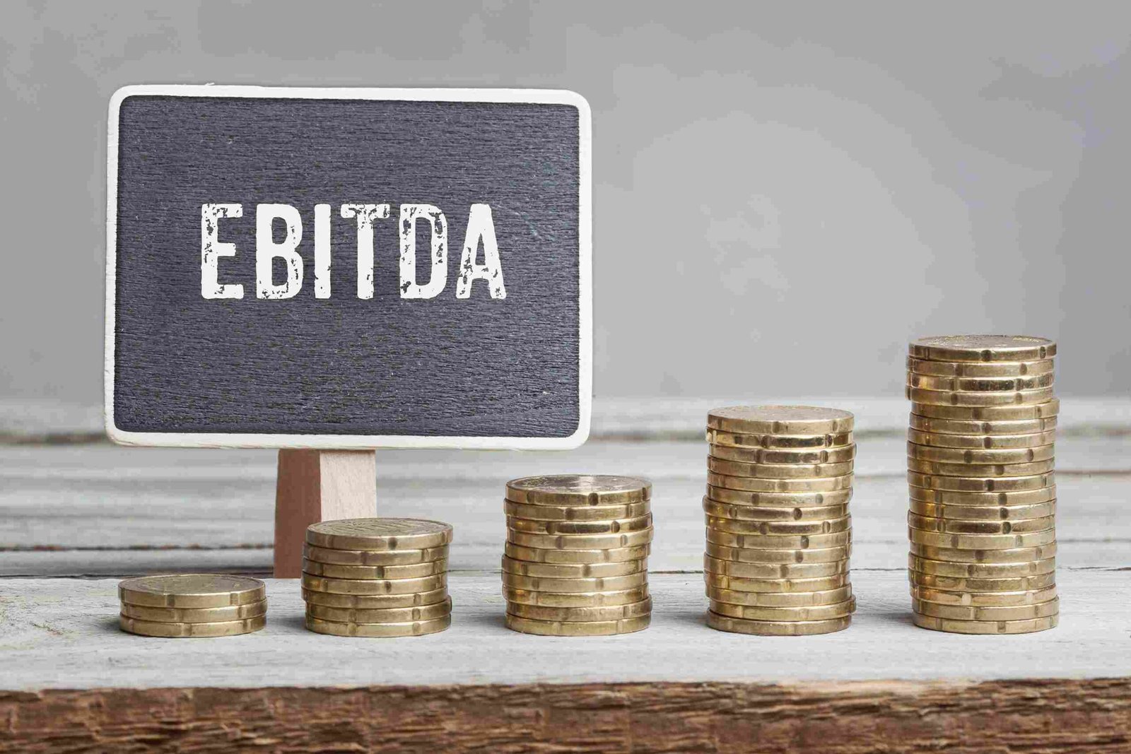 Stacks of coins increasing in height next to a small sign labeled EBITDA