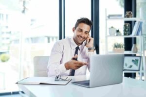 Professional speaking on the phone while working on a laptop in an office, representing the role of a portfolio manager