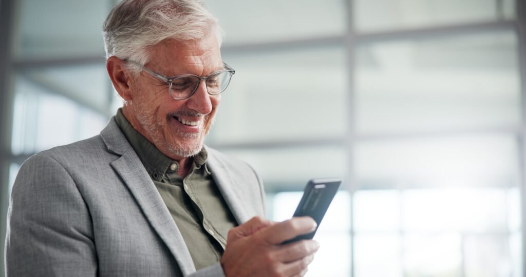 A professional in business attire smiling while checking a smartphone in an office setting