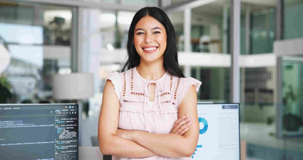 Smiling financial analyst standing confidently in a modern office with computer screens displaying financial data