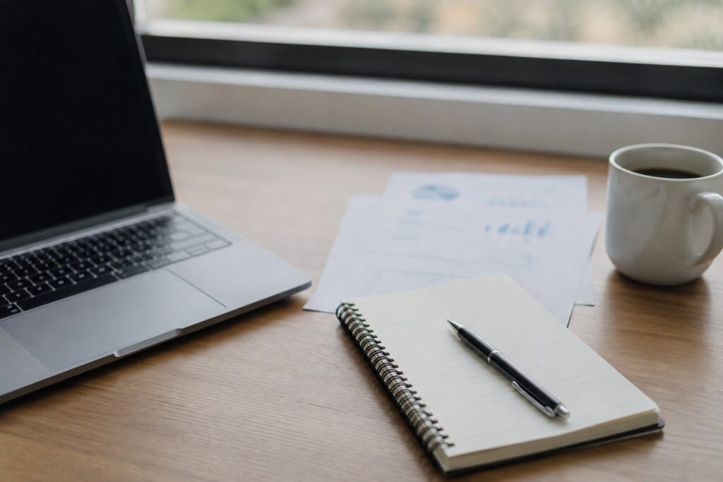 Laptop, notebook, coffee, and financial reports on a desk.