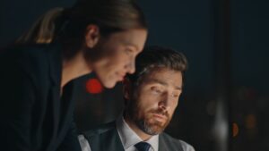 Two finance professionals review data on a screen in a dark office
